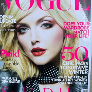 Può includere: Un numero di novembre della rivista Vogue con un ritratto di copertina di Sophie Dahl. La copertina presenta titoli in testo rosa brillante come Denim Update, Pink! Winter's irresistible shade e 50 Chic Ways to Survive Winter, insieme a una sciarpa a pois bianchi e neri.