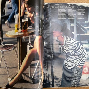 May include: A fashion magazine spread featuring two models in stylish outfits. One model is seated at a cafe table with a drink, while the other is standing, wearing a zebra-striped jacket and a checkered skirt. The text "A GEOMETRIE VARIABLE" is visible.