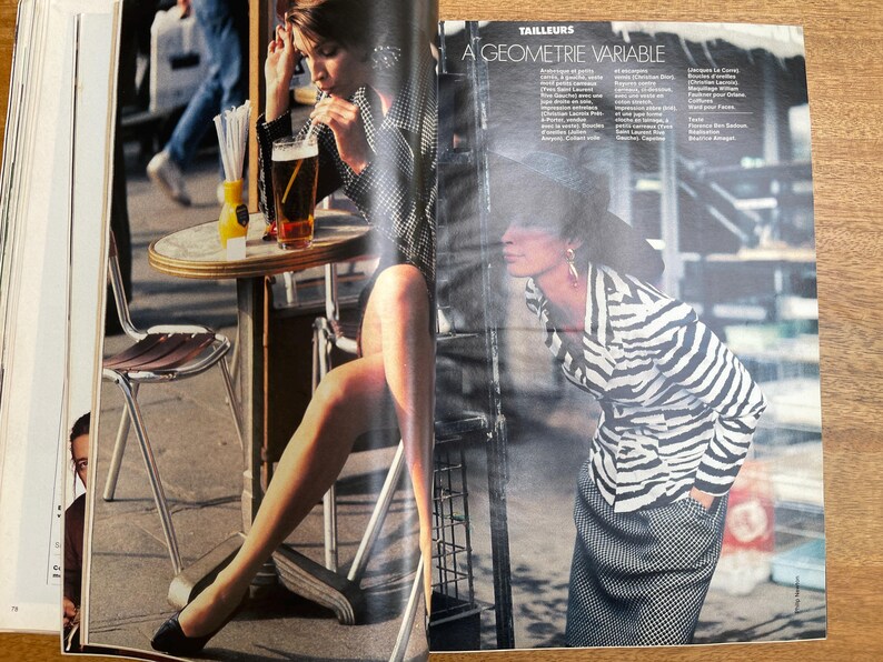 May include: A fashion magazine spread featuring two models in stylish outfits. One model is seated at a cafe table with a drink, while the other is standing, wearing a zebra-striped jacket and a checkered skirt. The text "A GEOMETRIE VARIABLE" is visible.