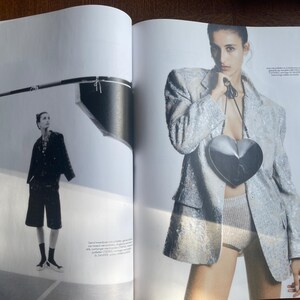 May include: A fashion editorial spread featuring a woman in a sequined blazer and a heart-shaped purse. The image is in black and white and colour, with a model in a studio setting. The model is also wearing shorts.