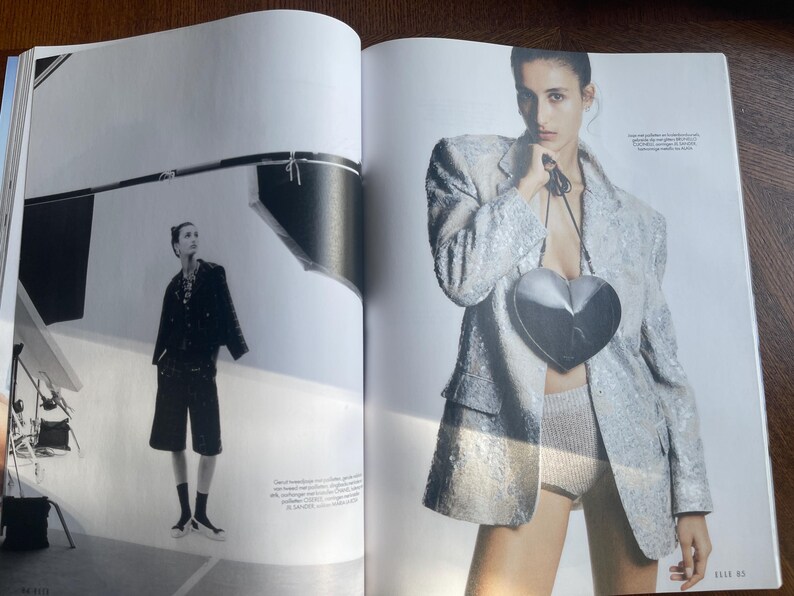 May include: A fashion editorial spread featuring a woman in a sequined blazer and a heart-shaped purse. The image is in black and white and colour, with a model in a studio setting. The model is also wearing shorts.