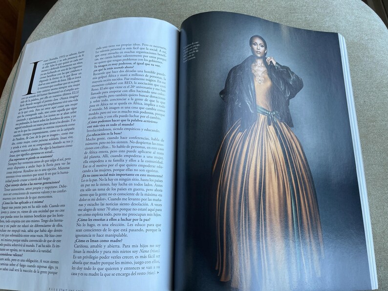 Puede incluir: Una p&aacute;gina de revista de moda con una modelo con un vestido largo y fluido de color amarillo dorado. La modelo lleva una chaqueta negra sobre una parte superior de color claro. El vestido tiene una falda ancha y est&aacute; ce&ntilde;ido a la cintura con una faja verde. El fondo es oscuro.
