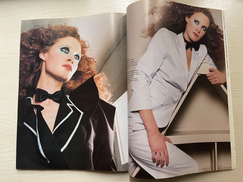 May include: Two women with red hair are wearing different styles of jackets. One woman is wearing a black jacket with a white trim and a black bow tie. The other woman is wearing a white jacket with a black bow tie. Both women are looking at the camera.