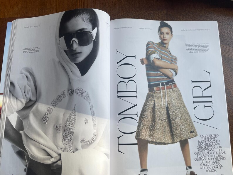 May include: A magazine spread with a model in sunglasses and a hoodie with the text "IT'S NOT ROCK N ROLL". The other model wears a striped shirt, pleated skirt, and the text "TOMBOY GIRL".