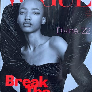 May include: Vogue Italia magazine cover featuring a woman with a nose ring and short hair. The cover has the text "VOGUE" in red at the top, with the text "Break The Dress Code" in red at the bottom. The text "Divine, 22" is also visible.