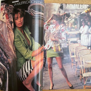 May include: A fashion magazine spread featuring two women in stylish outfits. One woman wears a green blazer and a black and white striped skirt. The other woman wears a floral jacket, a green skirt, and carries a small purse. The background shows a cafe setting.