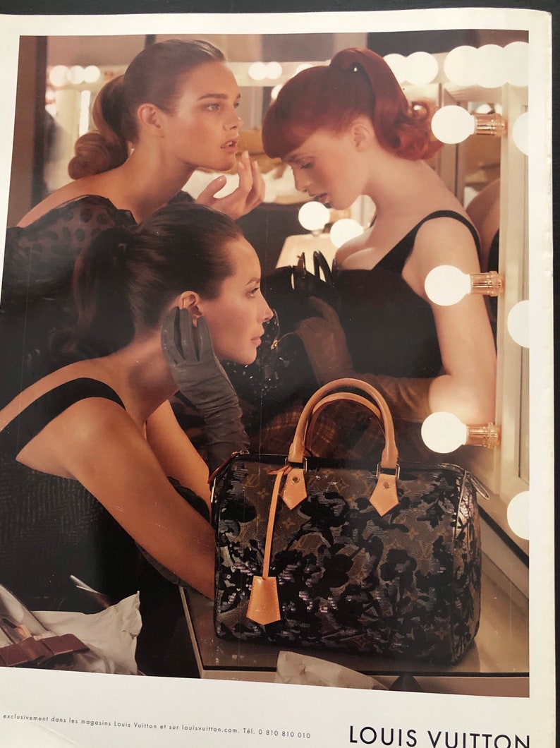 以下が含まれることがあります： 黒いドレスを着た3人の女性が、電球のついた鏡の前に立っています。手前にいる女性は黒い手袋をして、花柄の黒と茶色のルイ・ヴィトンのハンドバッグを持っています。