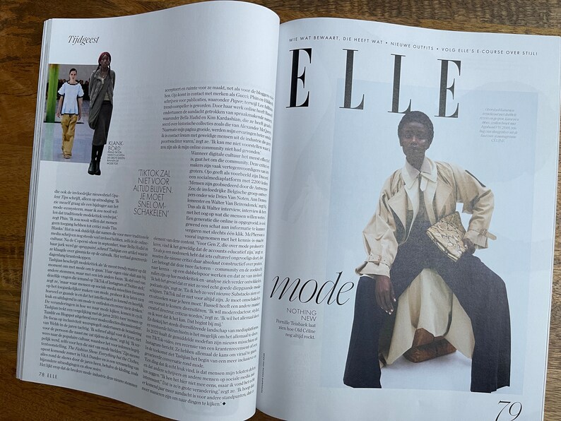 Puede incluir: Una portada de revista con la palabra "ELLE" en letras grandes y en negrita. La portada presenta a una modelo con un abrigo beige y pantalones oscuros, sentada en un taburete blanco. La modelo sostiene un peque&ntilde;o embrague estampado. El t&iacute;tulo de la revista es "mode" y el texto "NOTHING NEW" est&aacute; debajo.
