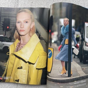 Puede incluir: Una revista de moda con una mujer con una chaqueta amarilla y otra con un abrigo azul con cuello de piel. Una est&aacute; frente a un sem&aacute;foro, la otra camina por una calle.