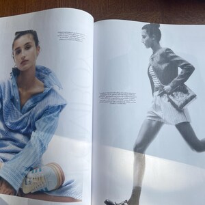 May include: A double-page spread from a fashion magazine. One model is seated, wearing a blue striped shirt and trainers. The other model is in motion, wearing a striped top, shorts, a jacket, and carrying a purse.