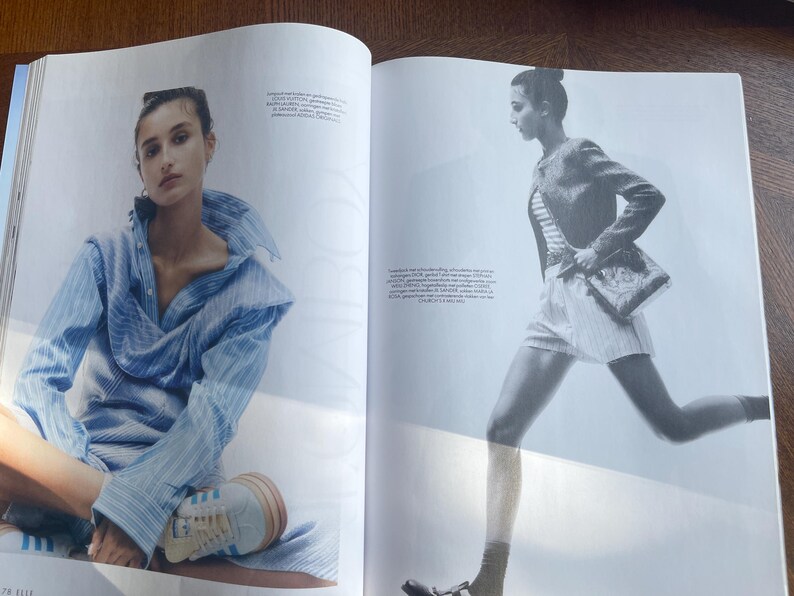 May include: A double-page spread from a fashion magazine. One model is seated, wearing a blue striped shirt and trainers. The other model is in motion, wearing a striped top, shorts, a jacket, and carrying a purse.
