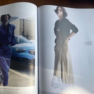 May include: A double-page spread from a fashion magazine. One model is in a blue denim ensemble, the other in a black jacket and a long beige skirt. A blue car and a white wall are visible in the background.