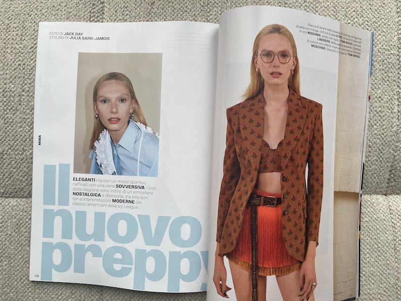 Puede incluir: Una p&aacute;gina de revista de moda con una modelo luciendo una blazer marr&oacute;n con estampado floral, combinada con un top corto a juego y una falda naranja. El texto "nuovo preppy" se muestra en letras grandes de color azul claro. Una imagen m&aacute;s peque&ntilde;a muestra a una modelo con una camisa azul claro.