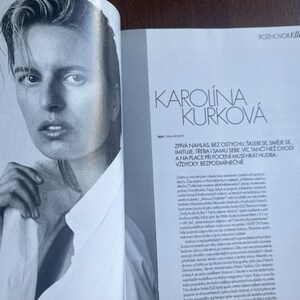 May include: Black and white magazine spread featuring a portrait of Karolina Kurkova. She is wearing a white collared shirt and a ring. The magazine page includes the text "ROZHOVOR Elle" and "KAROLINA KURKOV&Aacute;".