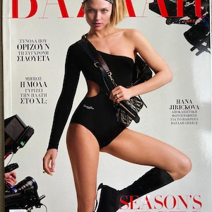Könnte beinhalten: Ein Modemagazin-Cover mit dem Wort "BAZAAR" in Rot. Das Cover zeigt eine Frau in einem schwarzen One-Shoulder-Body und einem Stirnband. Der Text "SEASON'S BESTS" steht in Rot am unteren Rand des Covers.