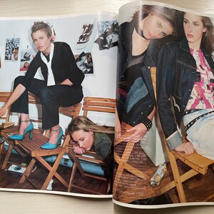 May include: Two women are sitting on wooden chairs. One woman is wearing a black jacket and blue jeans, and the other woman is wearing a denim jacket and jeans. Both women are wearing blue shoes.