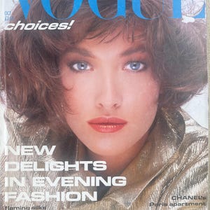 Può includere: Un numero vintage di ottobre della rivista Vogue con un ritratto in copertina di una persona con capelli castani corti e occhi azzurri. Il testo della copertina include VOGUE, choices!, NEW DELIGHTS IN EVENING FASHION e vari titoli di articoli.