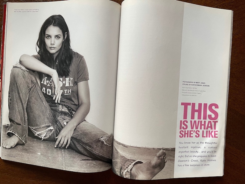 May include: A black and white photo of a woman sitting on the ground wearing blue jeans and a t-shirt with the text "M*A*S*H 40*TH" printed on it. The text "This is what she's like" is printed in pink on the right side of the image.