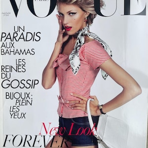 May include: A Vogue Paris magazine cover featuring a person wearing a red and white gingham top, a black and white patterned neck scarf with Dior text, and dark blue shorts. The person holds a white handbag. The cover includes text like Vogue, Un Paradis Aux Bahamas, Les Reines Du Gossip, Bijoux: Plein Les Yeux, New Look Forever, and Le Classique De Christian Dior Remixé.
