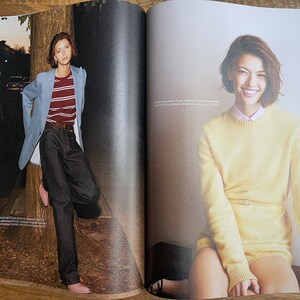 Puede incluir: Dos mujeres son fotografiadas en un reportaje de revista. La mujer de la izquierda lleva una chaqueta azul claro sobre una camisa a rayas y unos vaqueros azul oscuro. La mujer de la derecha lleva un jersey amarillo con cintur&oacute;n y una camisa blanca debajo.