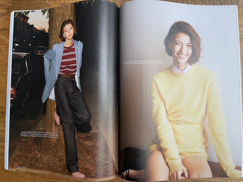 Puede incluir: Dos mujeres son fotografiadas en un reportaje de revista. La mujer de la izquierda lleva una chaqueta azul claro sobre una camisa a rayas y unos vaqueros azul oscuro. La mujer de la derecha lleva un jersey amarillo con cintur&oacute;n y una camisa blanca debajo.