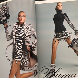 以下が含まれることがあります： 2人のモデルがシマウマ柄の服を着て、シマウマ柄のバッグを持っています。左側のモデルはシマウマ柄のコートとドレスを着ています。右側のモデルは黒いタートルネックとシマウマ柄のスカートを着ています。両方のモデルはシマウマ柄のブーツを履いています。
