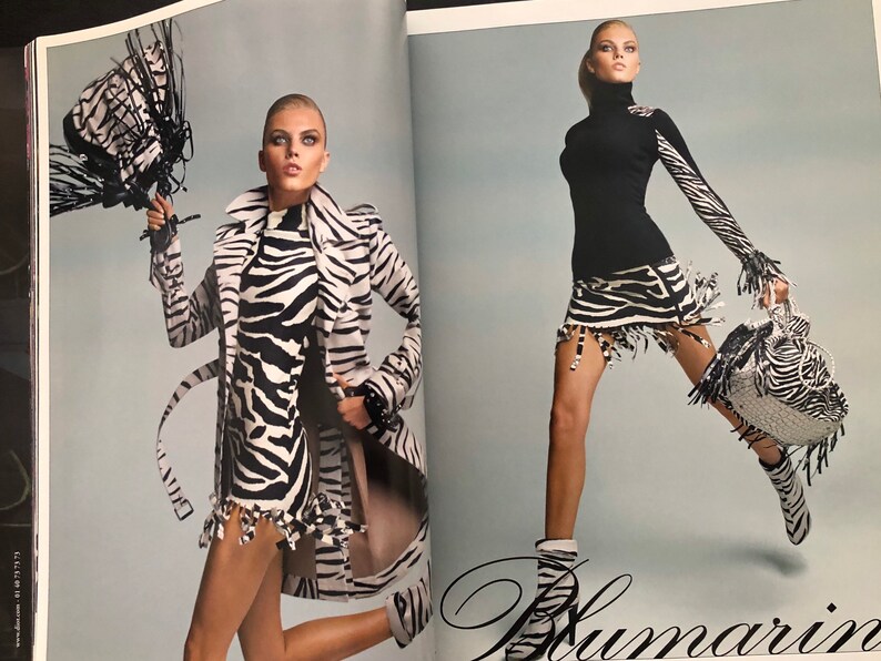 以下が含まれることがあります： 2人のモデルがシマウマ柄の服を着て、シマウマ柄のバッグを持っています。左側のモデルはシマウマ柄のコートとドレスを着ています。右側のモデルは黒いタートルネックとシマウマ柄のスカートを着ています。両方のモデルはシマウマ柄のブーツを履いています。
