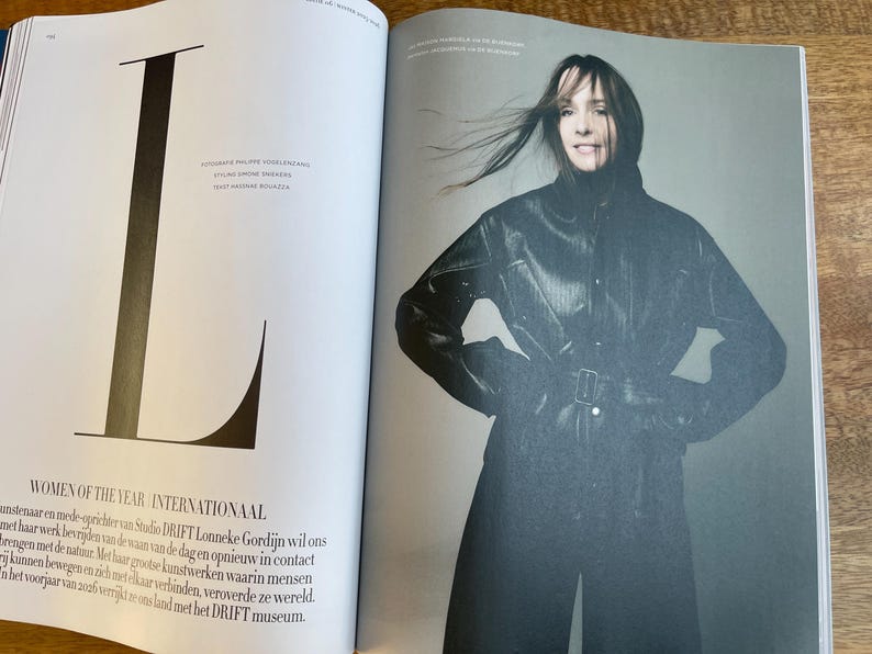 May include: A magazine spread featuring a woman in a black leather coat with a belt. The left page has a large black letter "L" and text that reads "WOMEN OF THE YEAR INTERNATIONAAL". The woman is smiling.