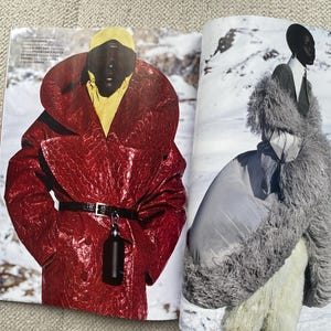 Puede incluir: Una revista de moda con dos modelos en atuendos de invierno. Una modelo lleva un abrigo rojo texturizado con cintur&oacute;n negro y un accesorio negro. La otra modelo lleva un abrigo de piel gris y un atuendo blanco, sobre un fondo nevado.