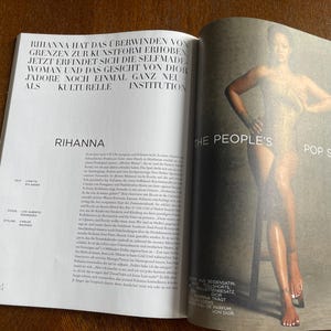 Puede incluir: Una revista de doble p&aacute;gina con una imagen de cuerpo entero de una persona posando sobre un taburete. El texto "THE PEOPLE'S POP STAR" es visible. La p&aacute;gina izquierda tiene texto en alem&aacute;n, con el nombre "RIHANNA" en un lugar destacado.