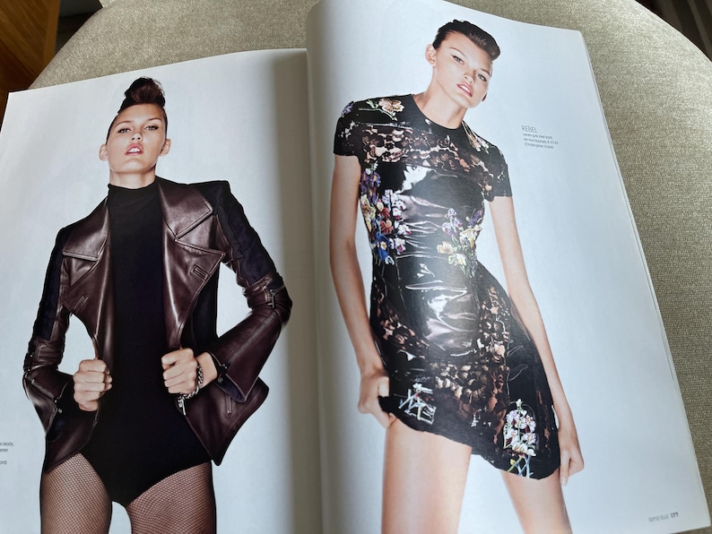 May include: Two-page spread from a fashion magazine featuring a model in two different outfits. On the left, a brown leather jacket with black accents and a black bodysuit. On the right, a black dress with a floral pattern.