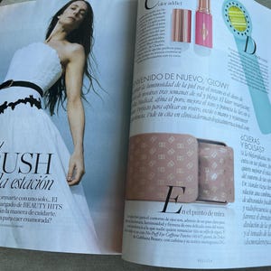 Puede incluir: Una p&aacute;gina de revista de moda con una mujer con un vestido blanco de un solo hombro con cintur&oacute;n negro y detalles de encaje. El texto "Tu CRUSH de la estaci&oacute;n" es visible, junto con otros textos y productos de belleza.