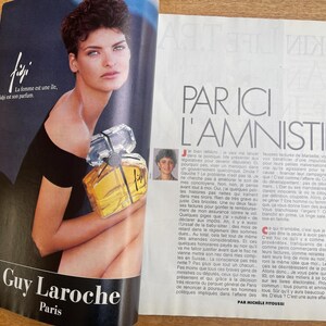 May include: Magazine advertisement for Guy Laroche Paris perfume, featuring a woman holding a perfume bottle. The bottle is clear with a yellow liquid and a silver cap. The text "Fiji" and "La femme est une &icirc;le, Figi est son parfum" are visible.