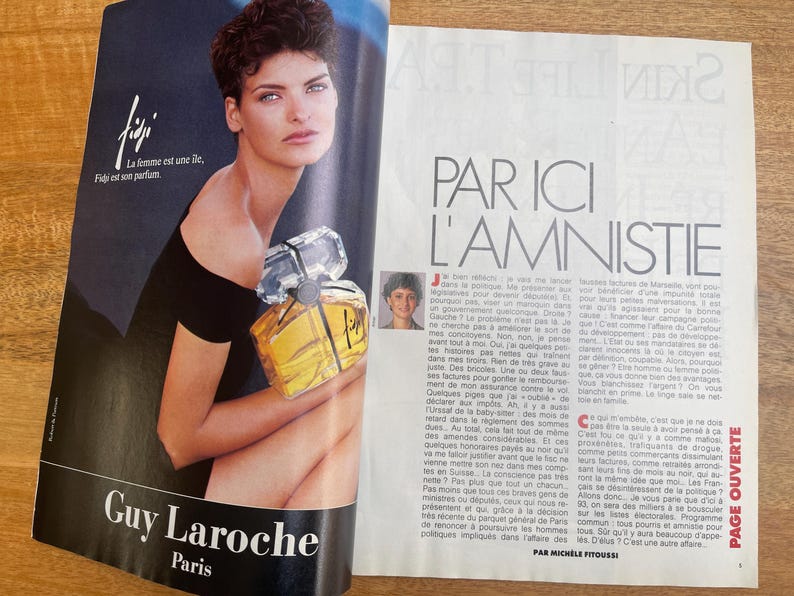 May include: Magazine advertisement for Guy Laroche Paris perfume, featuring a woman holding a perfume bottle. The bottle is clear with a yellow liquid and a silver cap. The text "Fiji" and "La femme est une &icirc;le, Figi est son parfum" are visible.