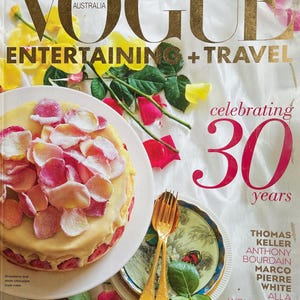 May include: A Vogue Australia magazine cover featuring a white chocolate and strawberry layer cake decorated with rose petals. The cover text reads "Celebrating 30 Years" and lists the names of chefs including Thomas Keller, Anthony Bourdain, and Marco Pierre White.