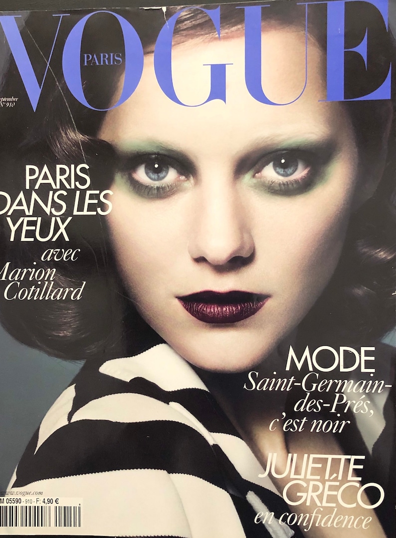 以下が含まれることがあります： マリオン・コティヤールを表紙に迎えたヴォーグ誌。緑のアイシャドウと濃い赤のリップをつけたマリオン・コティヤール。表紙のテキストは「パリ・ダン・レ・ジュー」と「モード・サンジェルマン・デ・プレ、セ・ノワール」で、ジュリエット・グレコが自信を持って語っている。
