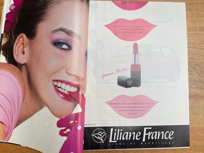 May include: An advertisement for Liliane France makeup. The image features a woman with bright pink lipstick and eye makeup. A lipstick tube and a small black compact are also shown. The text "Liliane France" is at the bottom.