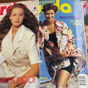 Op de afbeelding: Een stapel vintage modebladen. De covers tonen modellen in diverse outfits, waaronder een crèmekleurige blazer en een jasje met bloemenprint. De tijdschriften bevatten tekst in meerdere talen.