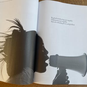 May include: Black and white photograph of a person speaking into a megaphone. The person's silhouette is visible, with their mouth open and the megaphone pointed forward. The text on the page reads: "Ik geloof in leiderschap met empathie. Ondernemen met empathie. Dat is de verbinding die we nodig hebben."