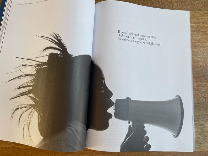 May include: Black and white photograph of a person speaking into a megaphone. The person's silhouette is visible, with their mouth open and the megaphone pointed forward. The text on the page reads: "Ik geloof in leiderschap met empathie. Ondernemen met empathie. Dat is de verbinding die we nodig hebben."