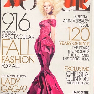Può includere: Una copertina di rivista con Lady Gaga che indossa un abito rosa con un'ampia acconciatura afro bionda. La rivista è Vogue, e il testo della copertina recita "916 Pages of Spectacular Fall Fashion for All. Think You Know Lady Gaga? Think Again." La copertina presenta anche il testo "Special Anniversary Issue 120 Years of Style. The Stars, The Models, The Editors, The Designers. Exclusive Chelsea Clinton. An Inside Look. Hair is the New Makeup. Fall's Most Fearless Trend."