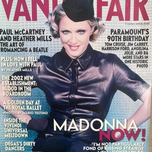 Puede incluir: Una portada de la revista Vanity Fair de octubre de 2002 con Madonna vistiendo una camisa de cuero negra y una gorra militar negra. La portada incluye titulares como Exclusive First Look: The New Harry Potter y Madonna Now!