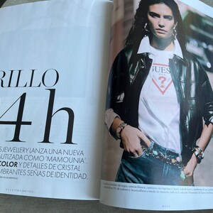 Puede incluir: Una revista de moda con una modelo que lleva una chaqueta de cuero negra sobre una camiseta blanca de Guess y vaqueros. El texto "BRILLO 24h" aparece en la p&aacute;gina izquierda. La modelo tambi&eacute;n lleva joyas.