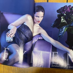 May include: A woman wearing a black sequined strapless dress and a silver clutch poses on a purple sofa. She has dark hair and red lipstick. A bouquet of dark purple roses in a black vase is in the background. The text "Sonbahar - Kis 2009-10" is visible in the bottom right corner.