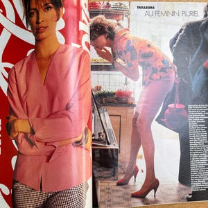 May include: A fashion magazine spread featuring two women. One woman is wearing a pink blouse and checkered pants. The other is wearing a floral print outfit and red heels. The magazine has French text.