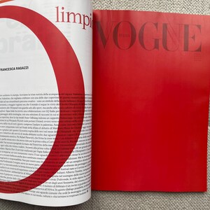 Puede incluir: P&aacute;ginas de revista abiertas con texto y un gran gr&aacute;fico rojo. La p&aacute;gina derecha es de color rojo liso con la palabra "VOGUE" en letras grandes. La p&aacute;gina izquierda tiene texto y un gr&aacute;fico rojo.