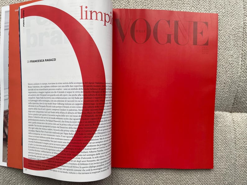 Puede incluir: P&aacute;ginas de revista abiertas con texto y un gran gr&aacute;fico rojo. La p&aacute;gina derecha es de color rojo liso con la palabra "VOGUE" en letras grandes. La p&aacute;gina izquierda tiene texto y un gr&aacute;fico rojo.