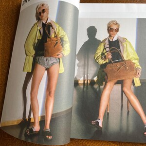 Puede incluir: Una p&aacute;gina de editorial de moda con una modelo con una chaqueta amarilla, un top negro y pantalones cortos grises. La modelo sostiene un bolso de mano de ante marr&oacute;n y lleva sandalias negras. El fondo es de color neutro.