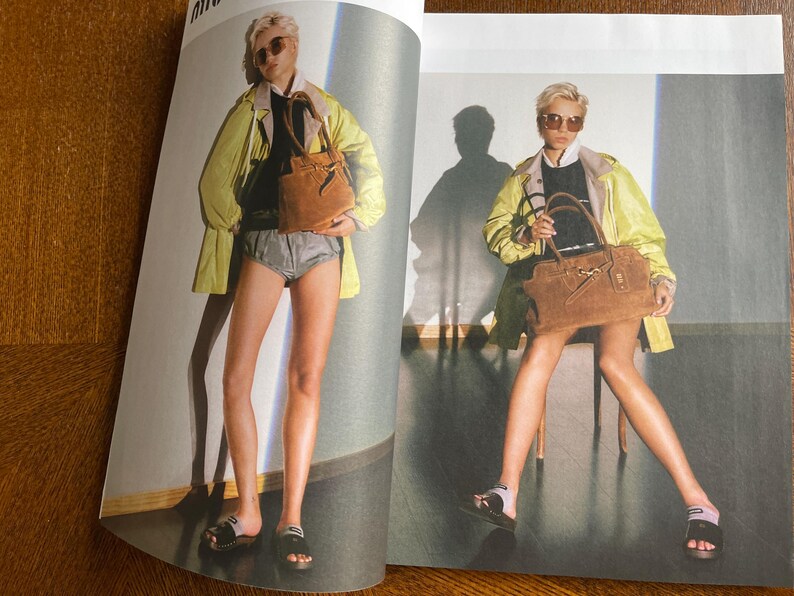 Puede incluir: Una p&aacute;gina de editorial de moda con una modelo con una chaqueta amarilla, un top negro y pantalones cortos grises. La modelo sostiene un bolso de mano de ante marr&oacute;n y lleva sandalias negras. El fondo es de color neutro.