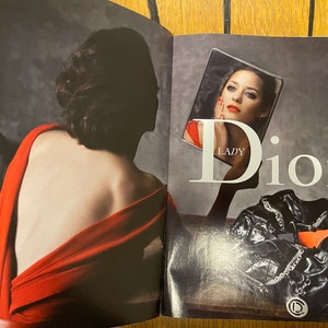 May include: A woman in a red dress looks into a mirror, the reflection shows a woman with red lipstick and the text "Lady Dior".